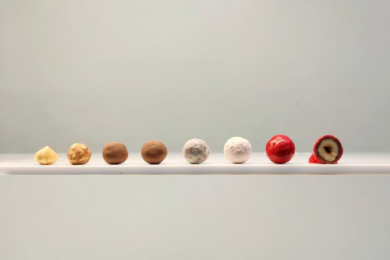 Several layers of various coatings of chocolate, caramel, milk chocolate, white chocolate and vibrant red coloured chocolate on hazelnut and all visible when coated hazelnut cut in half. Absoluetly delicious, made possibe by ChocoMan Spin from Mangharam